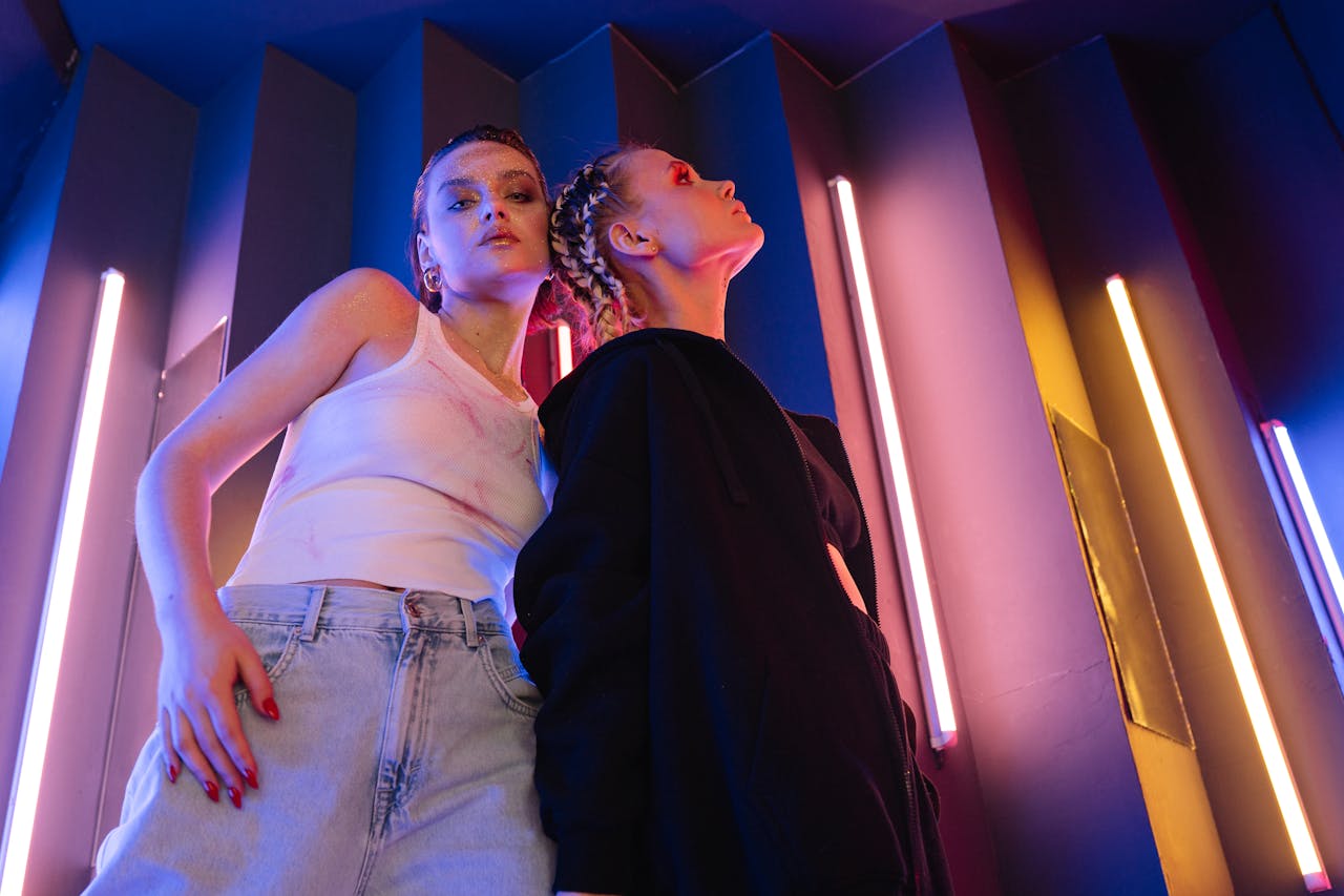 Two young women in a neon-lit urban environment, embodying modern youth culture.